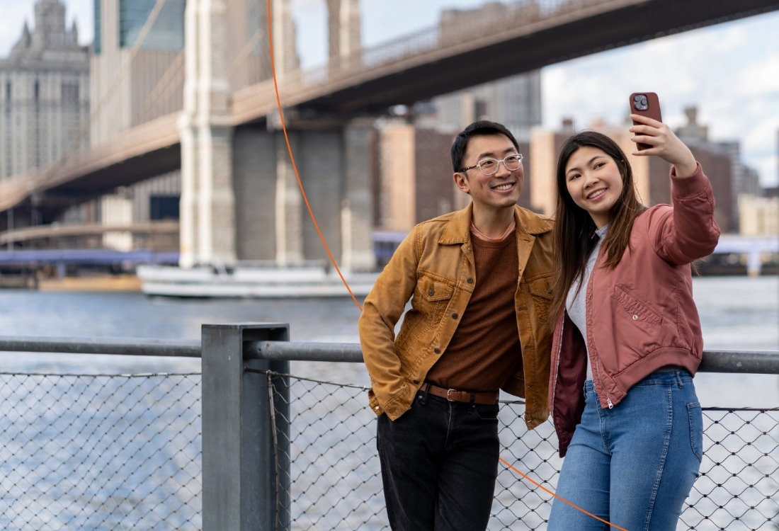 Man and woman taking a selfie with a bridge behind them. 